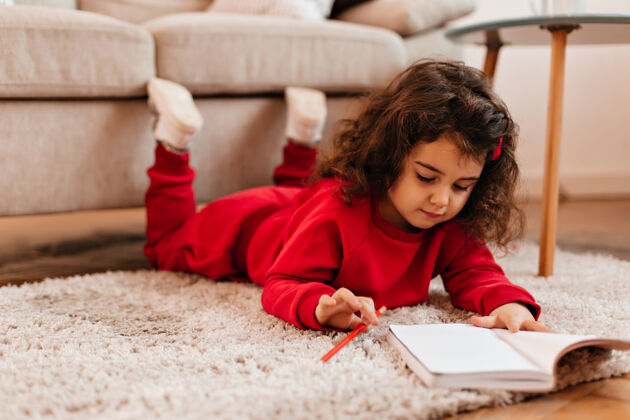 聪明在笔记本上集中儿童绘画室内拍摄的可爱的孩子躺在地毯上用笔女孩学习漂亮