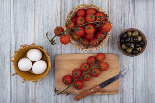 桶新鲜的葡萄藤西红柿的顶视图在一个木制的厨房板上用刀与葡萄藤西红柿在一个桶上和橄榄在一个灰色的木制背景木碗木材板用餐