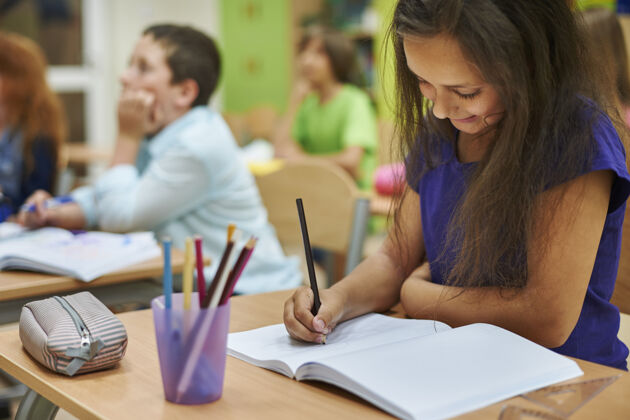 书桌在笔记本上画画的女孩小学生坐着低头
