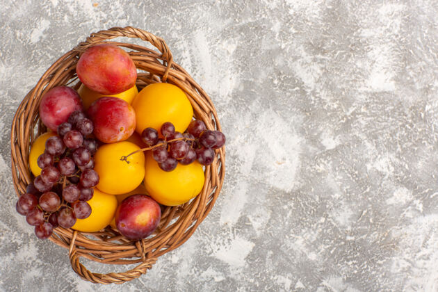 可食用的水果白色书桌上的篮子里放着新鲜甜美的杏子 李子和葡萄葡萄杏子篮子