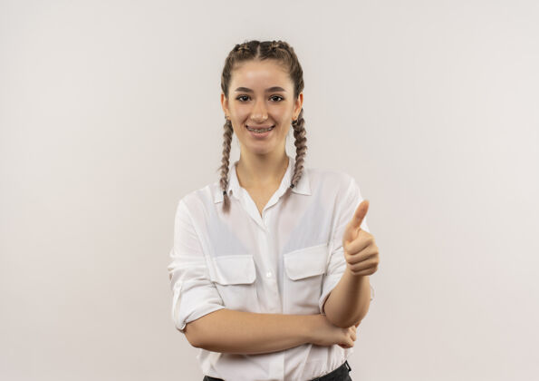 衬衫一个留着辫子 穿着白衬衫的年轻女学生站在白墙上 微笑着竖起大拇指望着前面拇指人微笑