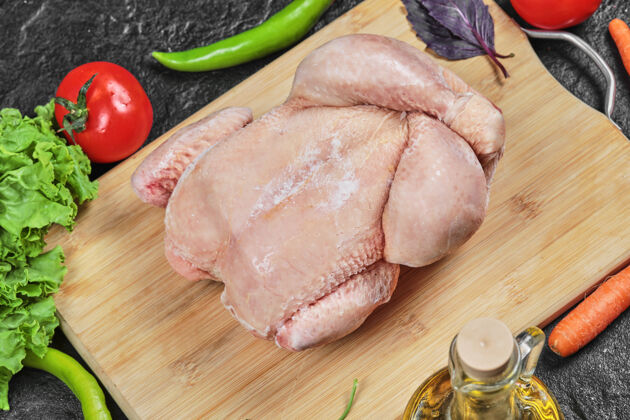 大蒜生的整只鸡放在木板上 里面有生菜 胡椒 油和西红柿番茄生的翅膀