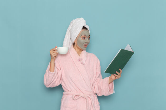 长袍正面图身着粉色浴袍的年轻女性淋浴后在蓝色墙壁上喝咖啡清洁美丽干净的水自我护理霜淋浴淋浴清洁前面