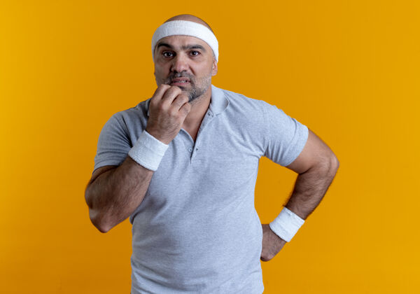 人戴着头巾的成熟的运动型男人望着站在橘色墙上的紧张紧张的咬指甲的前面姿势运动男人