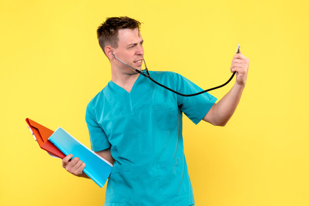 医生黄色墙上拿着文件和眼压计的男医生的正视图成人血压计医院