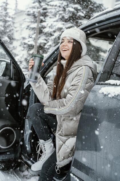 冒险侧视图笑脸女子享受雪 而在公路旅行自然女性饮料