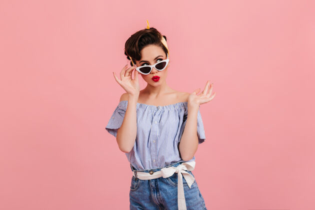 形状带着墨镜的沉思的小姑娘站在粉色的背景上一个穿着夏日套装的黑发年轻女士的摄影棚照片女孩服装老式