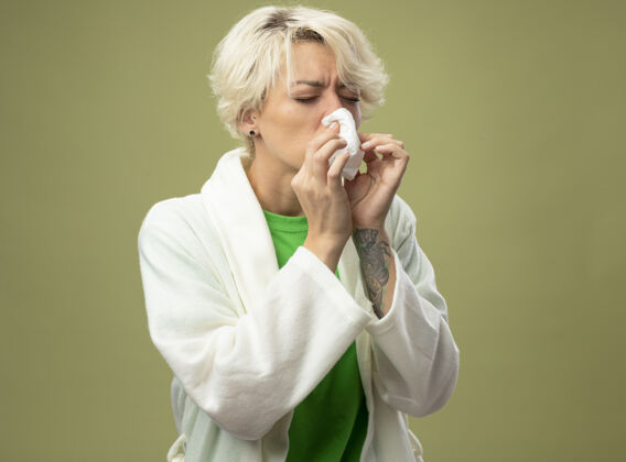 湿巾一个短头发的生病的女人站在光墙上用餐巾擦鼻子光短裤疾病
