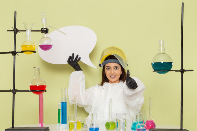 持有正面图身着特殊防护服的年轻女化学家手持绿色墙壁上的大白字化学实验室化学工作女科学化学化学实验室
