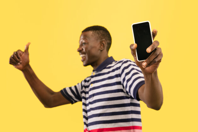 男孩年轻的非洲裔美国男子用智能手机隔离在黄色的工作室背景下 面部表情美丽的男性半身肖像人类情感的概念 面部表情幸运情绪男性