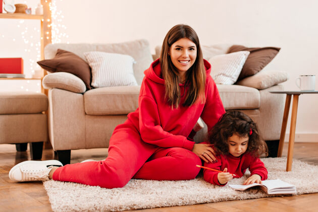 沙发笑着教女儿写字的年轻女子坐在地毯上的快乐妈妈和孩子的室内镜头积极女性女儿