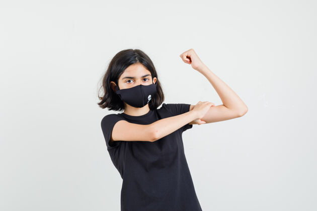年轻小女孩穿着黑色t恤 戴着面具 抱着手臂的肌肉 看起来很自信 前视图手臂和平漂亮