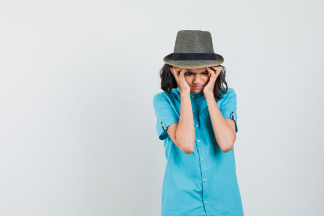 压力一位穿着蓝色衬衫 戴着帽子的年轻女士抱着她的太阳穴 看上去很紧张优雅积极黑发