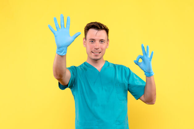 人黄墙上戴着蓝手套的男医生的正视图休闲快乐手套