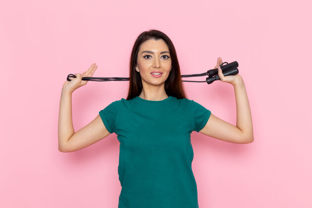 人正面图身着绿色t恤的年轻女性手持浅粉色墙壁上的跳绳腰部运动锻炼美丽苗条运动员绳子跳过观点