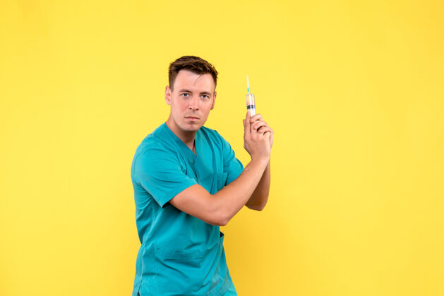 人黄色墙上拿着巨大针剂的男医生的正视图男人手持有