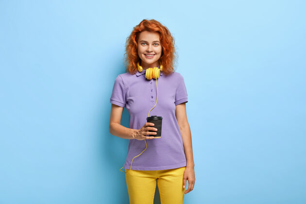 卡布奇诺照片中的少女喜欢热咖啡 拿着纸杯 通过耳机收听音频曲目饮用女性杯子