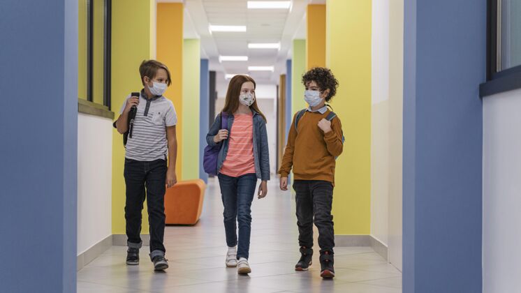 水平学校走廊上三个戴着医用口罩的孩子的正视图返校学生课堂