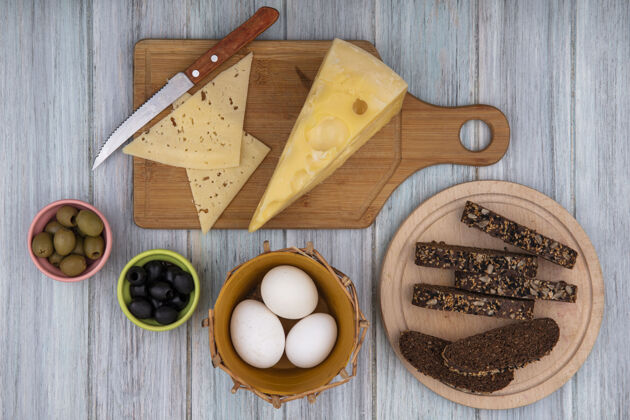 视图俯瞰图：鸡蛋放在篮子里 黑色面包片放在架子上 奶酪放在砧板上 刀子放在灰色背景上奶酪灰色支架