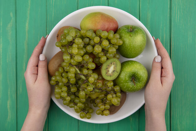 食物俯视图：一个女人拿着绿色的苹果 猕猴桃 绿色的葡萄和梨 放在绿色背景的盘子里绿色新鲜葡萄