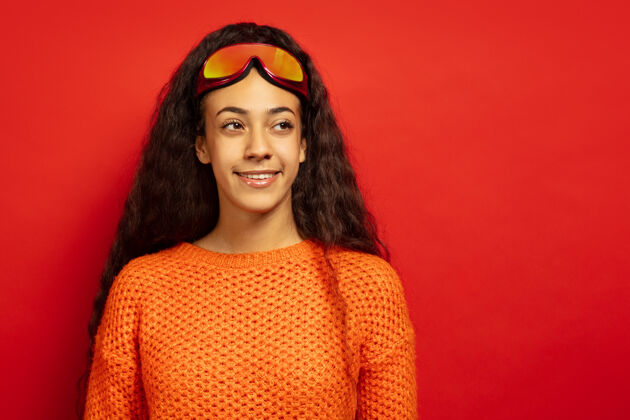 运动以红色工作室为背景 黑色皮肤的非洲裔美国年轻女子的滑雪面具肖像人类情感的概念 面部表情 销售 广告 冬季运动和假日微笑 看侧面欢呼非洲惊讶