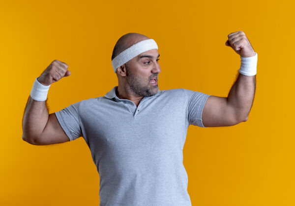 人戴着头巾的成熟运动型男子举手展示肱二头肌 站在橙色墙壁上的赢家概念人运动员运动装