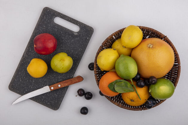 篮子俯瞰图：葡萄柚 橙子 酸橙和柠檬放在篮子里 樱桃李子和桃子放在砧板上 刀子放在白色背景上观点白新鲜