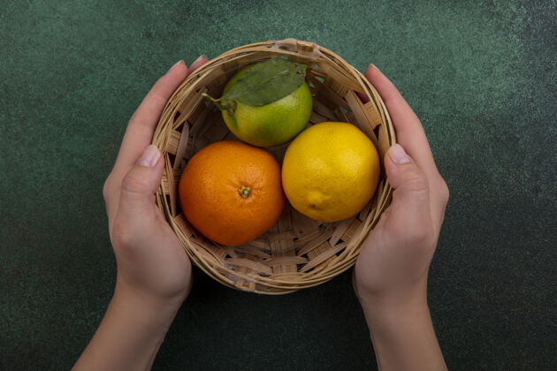 橙色俯视图：拿着篮子的女人 绿色背景上有橙色柠檬和酸橙五颜六色篮子酸橙