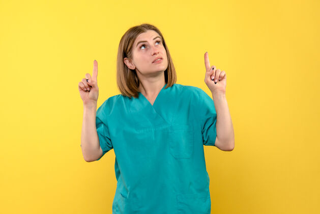 护士黄色墙壁上抬起手指的女医生的正视图手指女士肖像
