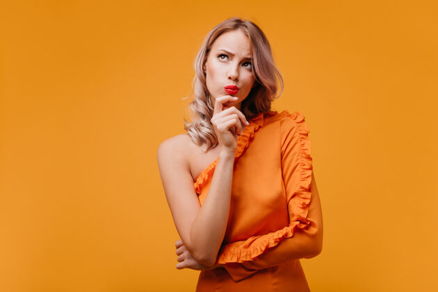年轻一个穿着橘色裙子的沉思的卷发女人抬起头来欢呼美丽时尚