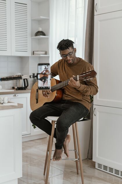 创意男音乐家在家里弹吉他和用智能手机录音的前视图乐器手音乐家房子