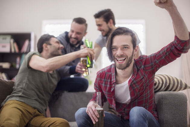 兴奋朋友们喝啤酒看足球赛家庭内部庆典冠军