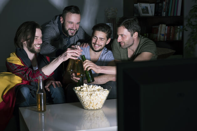 夜晚一群男人在电视上喝啤酒看足球庆典运动队酒精