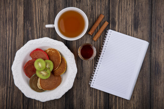 茶顶视图复制空间一杯茶与薄煎饼和猕猴桃片在一个盘子上与记事本和肉桂木背景盘子肉桂早晨