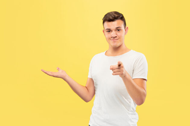人黄色工作室背景上的白人青年半身肖像穿着衬衫的漂亮男模人类情感的概念 面部表情 销售 广告指向和展示某物男性专业面部