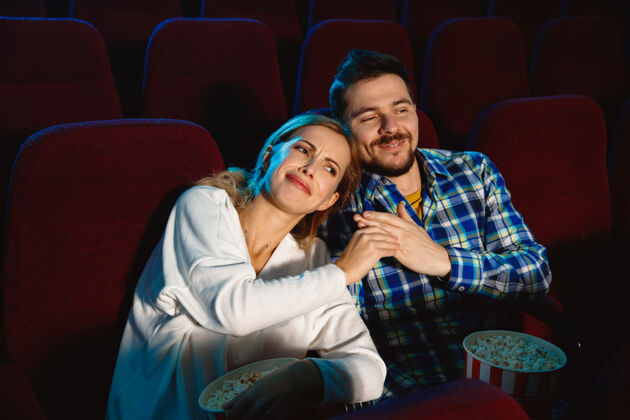 表达迷人的年轻白种人夫妇在电影院 房子或电影院看电影看起来富于表现力 惊讶和情绪化独自坐着玩关系 爱情 家庭 周末时间坐着电影情侣