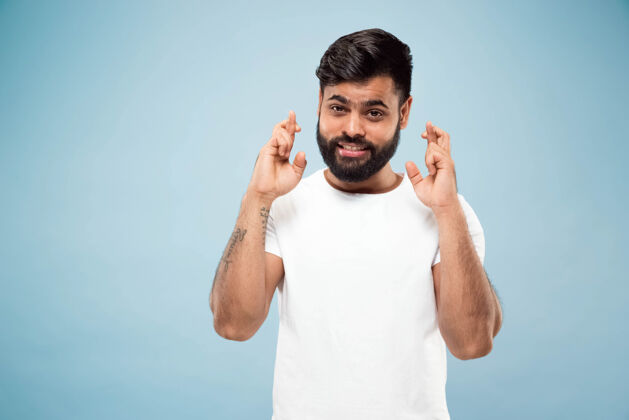 幸运蓝色背景上穿着白衬衫的印度教年轻人的半身特写肖像人类情感 面部表情 广告概念负面空间显示幸运的迹象 微笑事业男性高管