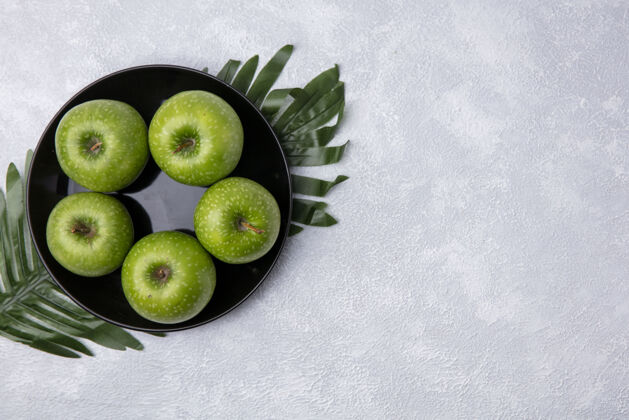 复制顶视图复制空间绿色的苹果在一个黑色的盘子上的树枝上 叶子在白色的背景上白色新鲜视图