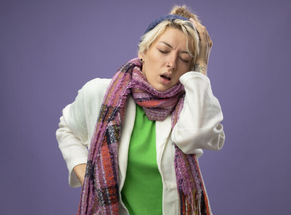生病有病的不健康的女人 短头发 戴着暖和的围巾和帽子 感觉不舒服 摸了摸她的头 患了流感 在紫色的背景下头痛得厉害温暖不健康围巾