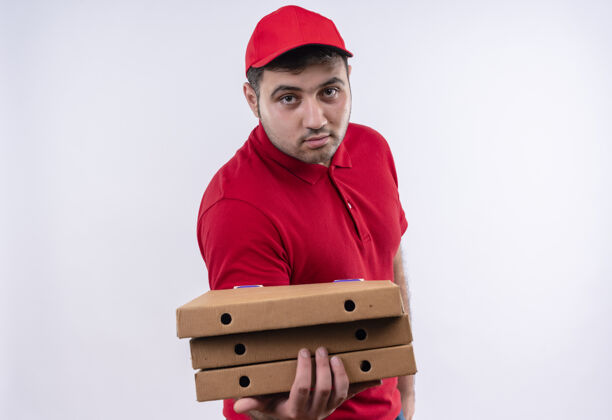 递送年轻的送货员身穿红色制服 头戴鸭舌帽 站在白墙上 脸上带着自信的微笑 端着披萨盒人脸年轻人