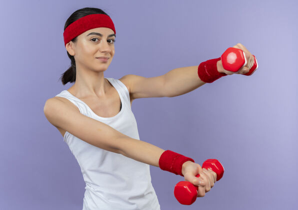 姿势穿着运动服的年轻健身女 头上戴着头带 手里拿着两个哑铃锻炼健康抱着