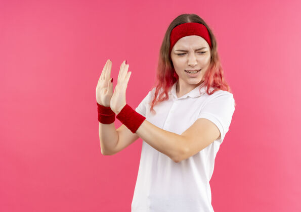 运动戴着头巾的年轻运动女郎站在粉红色的墙上 用厌恶的表情做着防卫的手势手势年轻人女人