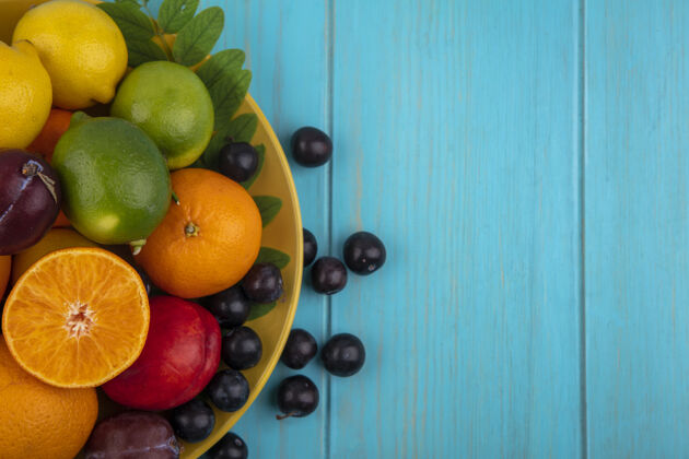 食物顶视图复制空间樱桃李子与橘子李子柠檬和酸橙在一个黄色的盘子上的绿松石背景景观柠檬橙色