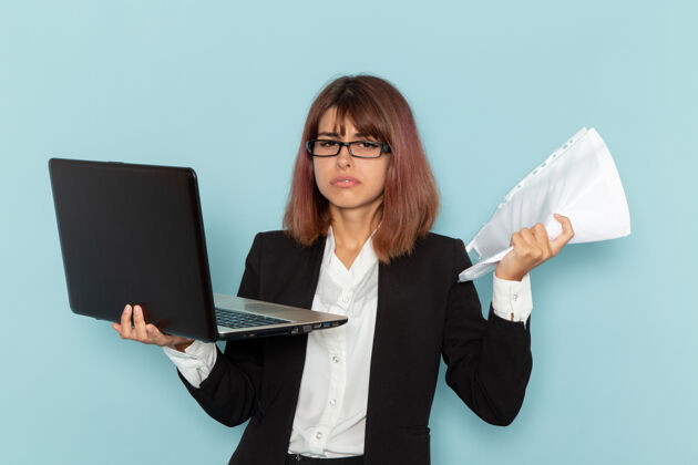 工作正面图：穿着西装的女上班族拿着纸和笔记本电脑在蓝色的表面上笔记本电脑电脑女