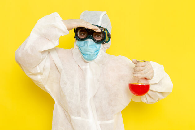 科学正面图穿着特殊防护服的男科学工作者拿着黄色表面上有红色溶液的烧瓶溶液套装特殊