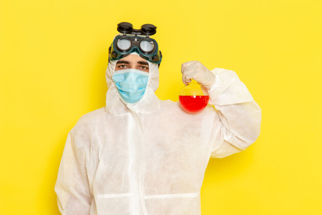 特殊正面图穿着特殊防护服的男科学工作者拿着黄色表面上有红色溶液的烧瓶科学男性服装