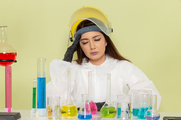 工作正面图：穿着特殊防护服的女化学家在绿色表面上工作和头痛头痛女特殊