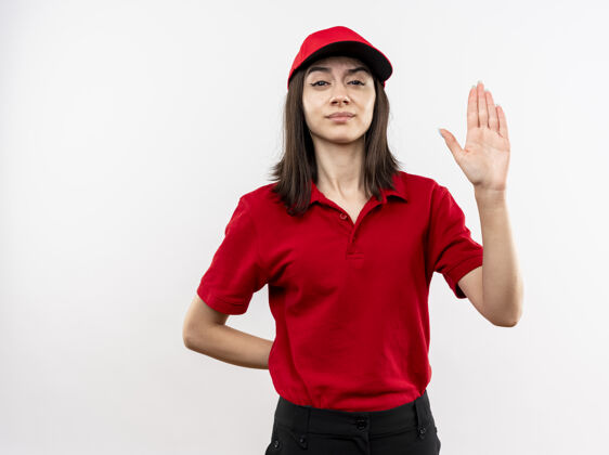 停止穿着红色制服 戴着帽子的年轻送货女孩看着镜头 严肃的脸上画着停止标志 张开的手站在白色的背景上手制服制造