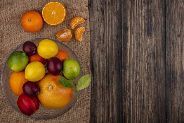复制顶视图复制空间水果混合柠檬 酸橙 李子 桃子和橘子在一个花瓶里 在木制背景上的米色餐巾上柠檬混合食物