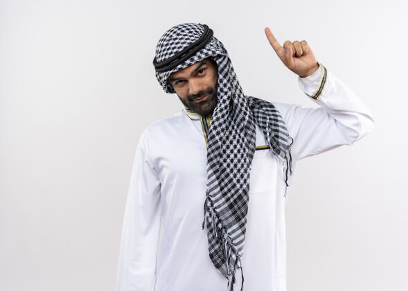 指向身着传统服装的阿拉伯男子自信地微笑着 食指竖立在白色的墙上手指站目录